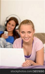 Smiling girls studying on laptop her sister listening music