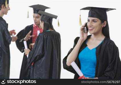 Smiling graduate student answering mobile phone with friends discussing against white background