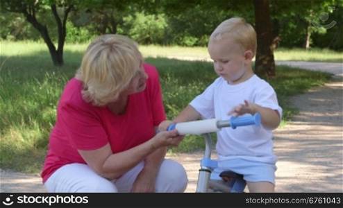 Smiling grandma learning her grandson to ride bicycle in park