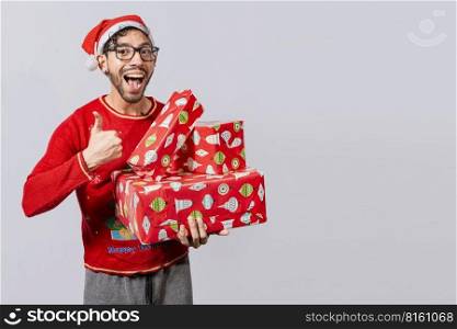 Smiling guy in christmas hat holding christmas gift boxes giving thumbs up. Friendly man in christmas clothes holding gift boxes, Christmas man holding gift boxes and smiling with thumb up