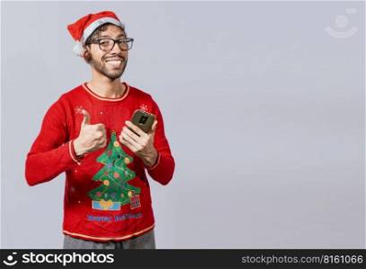Smiling guy in christmas hat using cellphone with thumb up. Smiling young man in christmas hat using cellphone and giving thumbs up. People in santa hat using phone and doing ok gesture