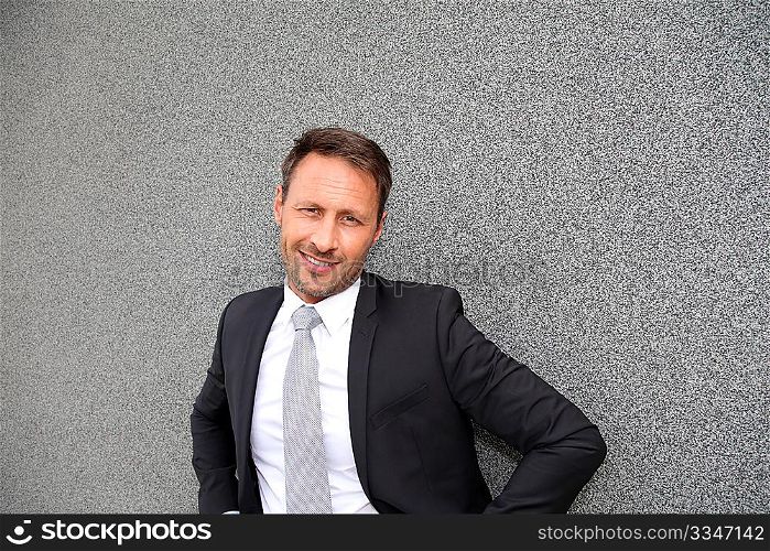 Smiling handsome businessman leaning on concrete wall