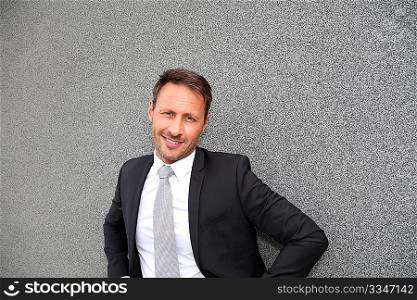 Smiling handsome businessman leaning on concrete wall
