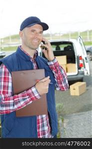 smiling handsome delivery man holding box and making call