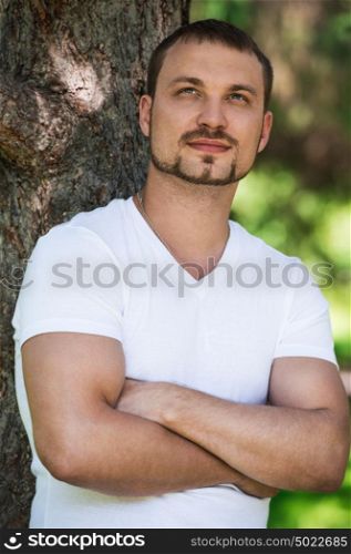 Smiling handsome man outdoors dreaming and leaning on tree. He is confident in his bright future