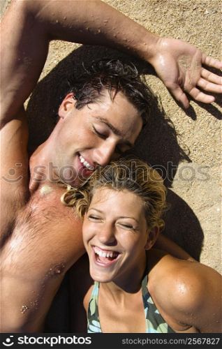 Smiling happy couple lying in sand on Maui, Hawaii beach.