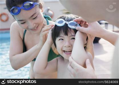 Smiling happy family helping son put on goggles by the poolside