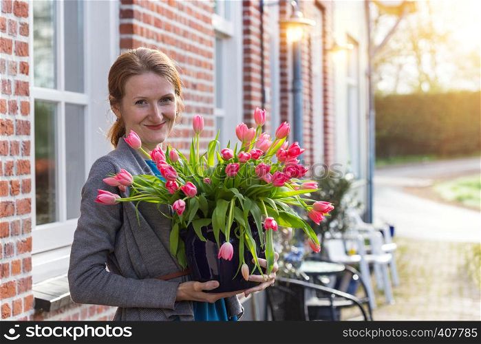 smiling happy girl holding a vase with pink tulips near with a traditional Dutch house. The Netherlands
