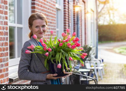 smiling happy girl holding a vase with pink tulips near with a traditional Dutch house. The Netherlands