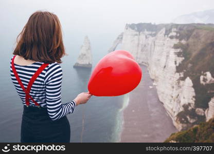 smiling happy girl with a red balloon in the shape of a heart at background of scenery Etretat. France