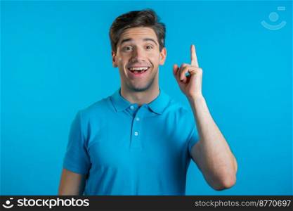 Smiling happy guy showing eureka gesture. Portrait of young man having idea moment pointing finger up on blue studio background. Smiling happy guy showing eureka gesture. Portrait of young man having idea moment pointing finger up on blue studio background. 