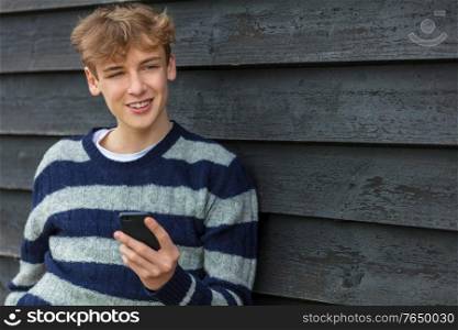 Smiling Happy male boy teenager outside leaning wall using his mobile cell phone for social media or video call