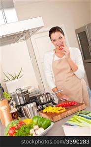 Smiling happy woman biting red pepper in the kitchen