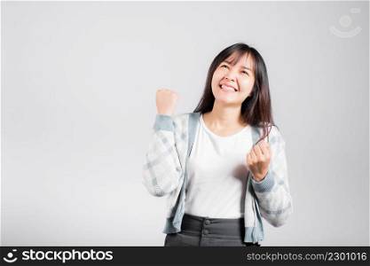 Smiling happy woman makes raised fists up celebrating her winning success gesture, Happy Asian beautiful young female excited say yes, studio shot isolated on white background with copy space