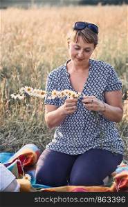 Smiling happy woman making coronet of wild flowers. Family spending time together on a meadow, close to nature. Candid people, real moments, authentic situations