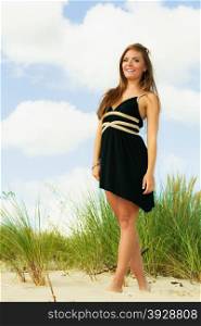 Smiling happy woman on beach. Young model in black dress outside.
