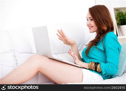 Smiling happy woman sitting on the sofa and using laptop at home