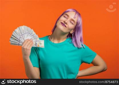Smiling happy woman with cash money - USD currency dollars banknotes on orange wall. Girl with violet dyed hairstyle. Symbol of jackpot, gain, victory, winning the lottery.. Smiling happy woman with cash money - USD currency dollars banknotes on orange wall. Girl with violet dyed hairstyle. Symbol of jackpot, gain, victory, winning the lottery