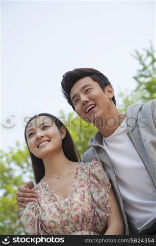 Smiling happy young couple with arm around the shoulders outdoors in a park, front view