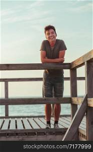 Smiling happy young man standing on a pier over the sea during summer vavations. Copy space room for text
