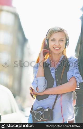 Smiling hipster girl listening music on city street