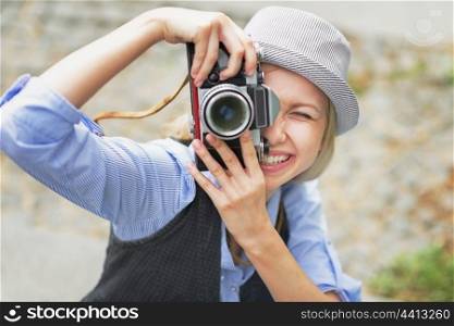 Smiling hipster girl making photo with retro camera