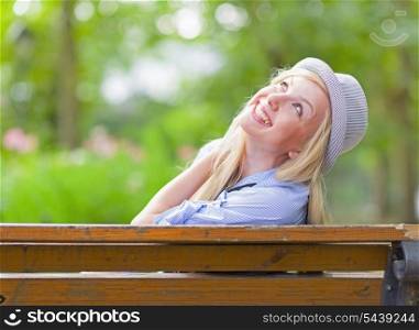 Smiling hipster girl sitting on bench in the city park and looking on copy space
