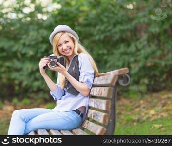 Smiling hipster girl with retro photo camera sitting on bench in the park