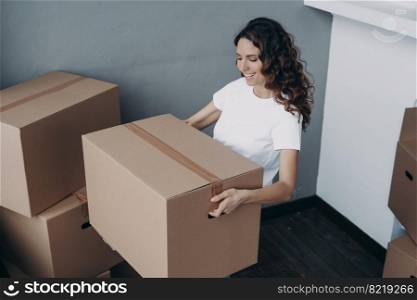 Smiling hispanic female homeowner renter holding packed cardboard box with personal belongings, moving in new home apartment. Happy girl brings things into rented house. Relocation, mortgage concept.. Smiling girl homeowner renter holding packed cardboard box, moving in new home apartment. Relocation