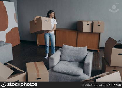 Smiling hispanic woman holding cardboard box, standing in living room, moving in new home. Happy female homeowner unpacking things in first own apartment. Bank loan and mortgage, tenancy concept.. Smiling woman holding cardboard box, moving in new home. Bank loan and mortgage, tenancy concept