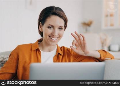 Smiling hispanic woman talking by video call at laptop, agree with friend, showing okay yes gesture. Happy female freelance worker makes ok sign, approving customer’s work task, accepting project.. Smiling hispanic woman showing okay yes gesture of agreement talking by video call at laptop