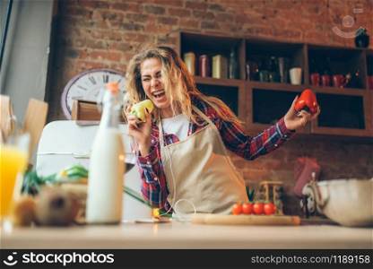 Smiling housewife in an apron plays with fresh pepper on the kitchen. Female cook making healthy vegetarian food, salad cooking. Housewife in an apron plays with fresh pepper