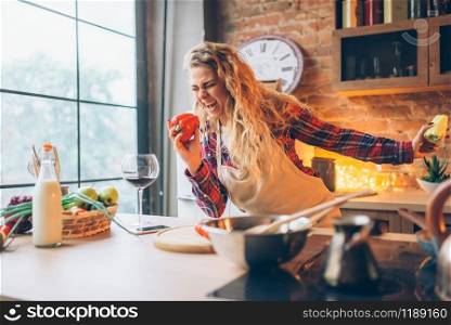Smiling housewife in an apron plays with fresh pepper on the kitchen. Female cook making healthy vegetarian food, salad cooking. Housewife in an apron plays with fresh pepper