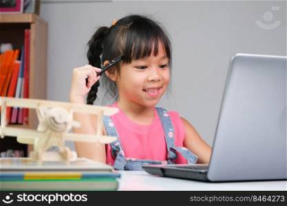 Smiling little Asian girl studying online having video call distant class with teacher using laptop. Happy girl learning English online with laptop at home. homeschooling concept