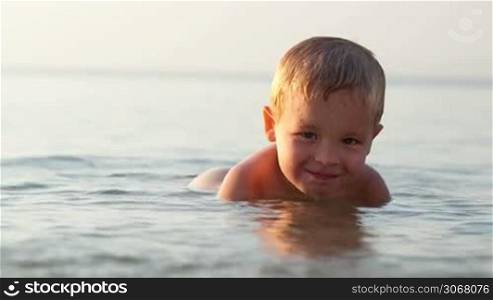Smiling little boy ducking down in the shallow water at the seaside in a tranquil ocean on a summer day