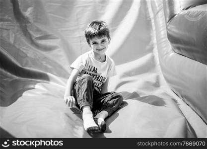 Smiling little boy playing on inflatable slide, looking at camera, black and white shot. Smiling little boy playing on inflatable slide, looking at camera