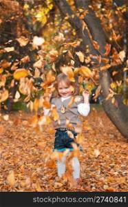 Smiling little girl (3 years) playing with dry autumn leaves. Evening in a park