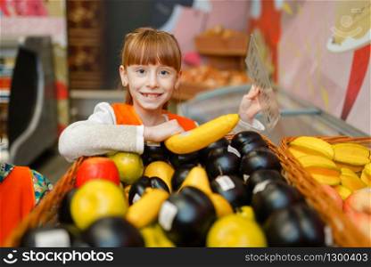 Smiling little girl in uniform playing saleswoman, playroom. Kids plays fruit sellers in imaginary supermarket, salesman profession learning