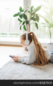 Smiling little girl listening music lying on the floor