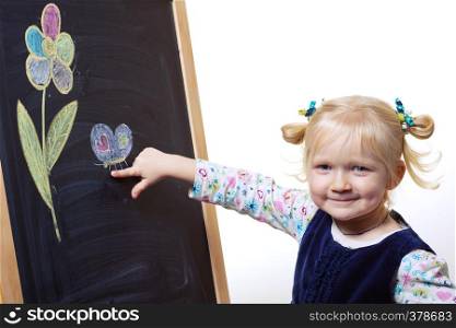 smiling little girl standing near blackboard on which are painted flower and butterfly