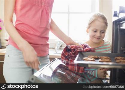 Smiling looking at mother removing cookie tray from oven at home