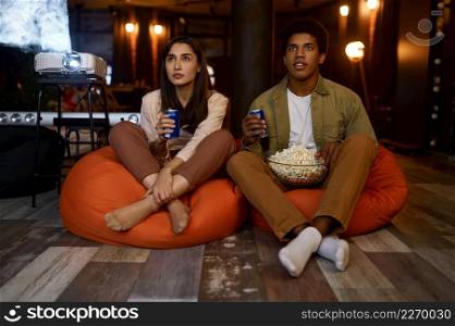 Smiling loving couple or friends watching movie at home. Man and woman drinking soda eating popcorn. Smiling loving couple or friends watching movie