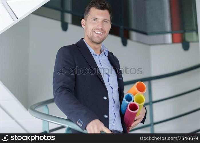 smiling male architect holding blueprints inside building