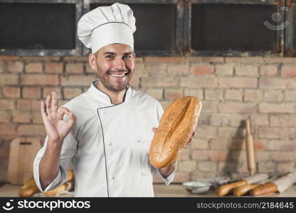 smiling male baker holding loaf showing ok hand sign gesture