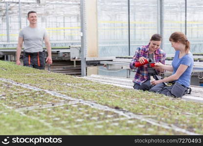 Smiling male botanist looking at female coworkers enjoying coffee break in greenhouse