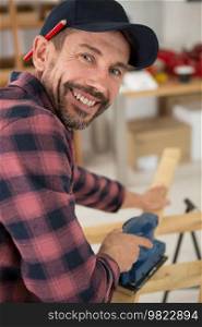 smiling male carpenter working with jigsaw at workbench