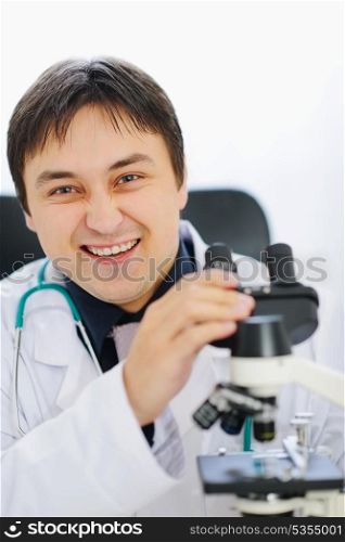 Smiling male doctor working with microscope