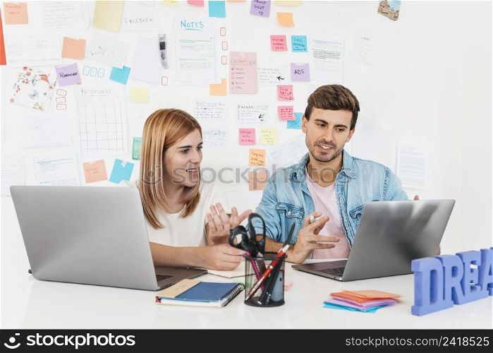 smiling male female sitting desk talking looking laptop