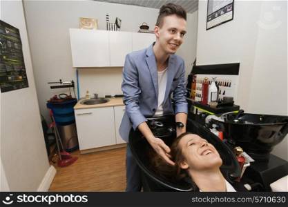 Smiling male hairstylist washing female customer&rsquo;s hair in salon