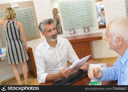 smiling male ophthalmologist and mature patient in modern optics store